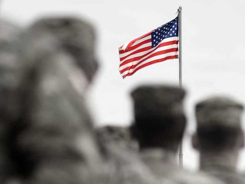 Military standing in front of an American flag, everything is blurry except the flag